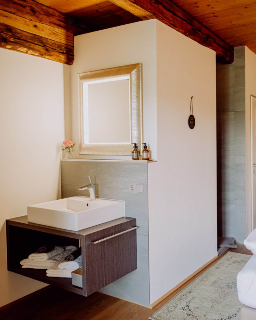 Offenes Badezimmer vom Weingartenzimmer, man sieht das Waschbecken samt Waschtisch und den beleuchteten Spiegel